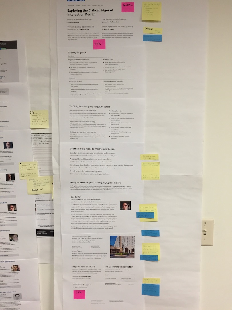 Paper prototypes hung on a wall marked up with critique on Post-in notes.